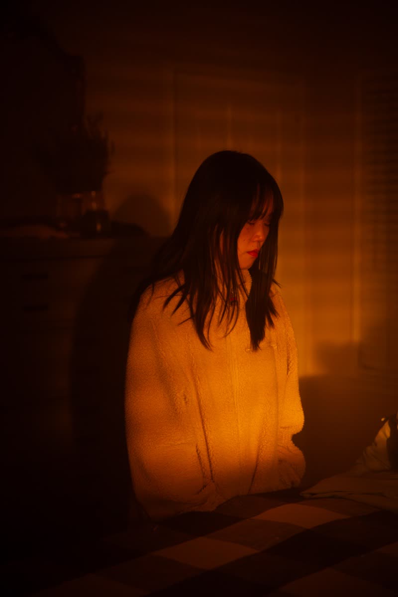 Alice Lee in deep amber light between takes, eyes down, the room glowing around her.